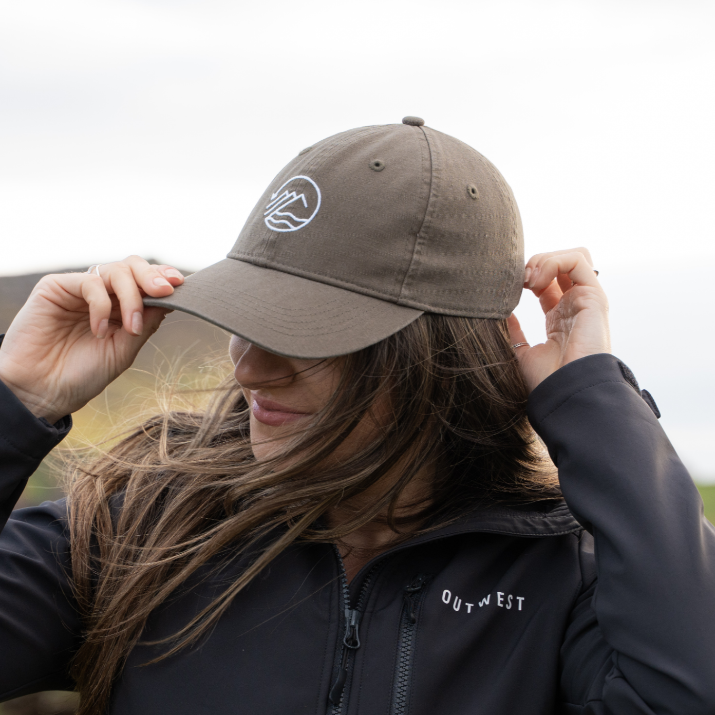 Person wearing a black jacket and dark green cap outdoors in a natural setting
